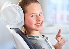 Smiling girl in dental chair giving thumbs up